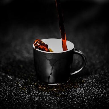 Close-up of steaming dark coffee being poured into a black cup on a dark textured surface. Rich aroma.